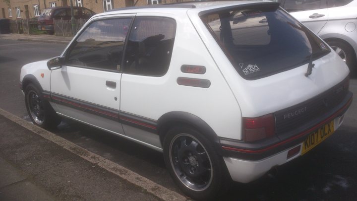 A white truck parked in a parking lot - Pistonheads - The image shows a white hatchback car parked on the side of a street. The car appears to be a small, compact model typical for urban use. The side mirrows and door handles are visible, and there is a smaller sticker on the rear window, along with a larger decal or sticker on the back window. The setting appears to be a residential area, possibly in the UK, given the style of the car and the license plate. It's a clear day, and there are houses with brick walls and Windows in the background.