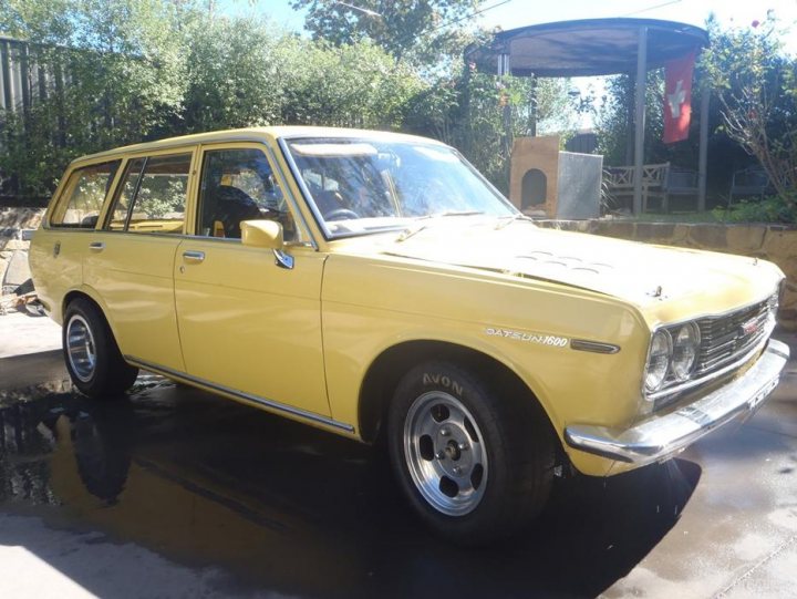 Lovely Cars: Interesting, Classic, Retro, Barge 5-10k - Page 60 - General Gassing - PistonHeads - The image shows a vibrant yellow Datsun pickup parked, with a rich, glossy appearance that suggests it might be well-maintained or restored. Its body is in good condition, and the car has a distinctive, somewhat menacing, blackout grill and large, shiny hubcaps. In the background, there are trees and a structure that looks like a pergola, adding to the park-like setting. The image conveys warmth with the bright yellow of the car against the softer colors of the surroundings.