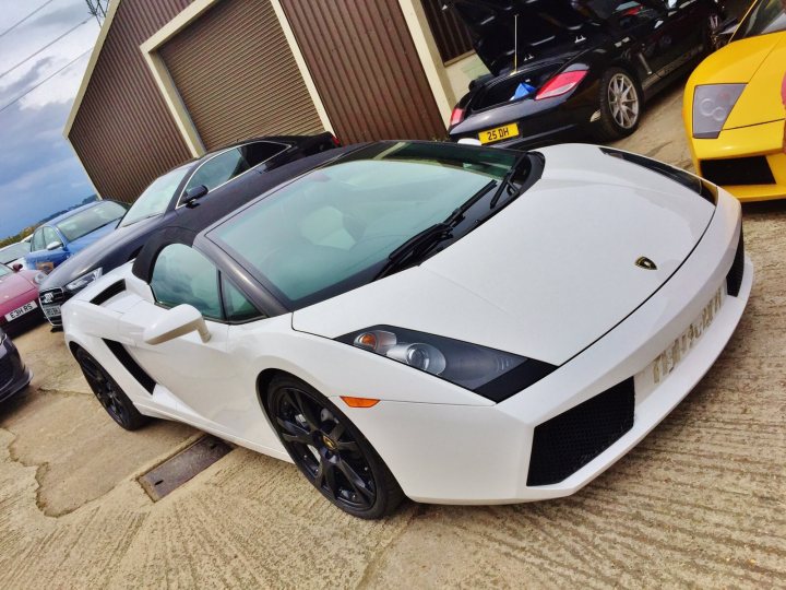 Newbie  - Page 1 - Gallardo/Huracan - PistonHeads - The image showcases a trio of sports cars parked in a gravel lot. A white Audi R8 V10 II, which is a convertible supercar, steals the lead as it is parked in front of two other luxury cars. The cars are parked nicely with the white Audi R8 facing the camera, making it the focal point. The nearest car also features the license plate number "HSKA", adding a personal touch to this luxury scene. The vehicles are parked in what appears to be a garage or warehouse setting, with a clear sky in the background.