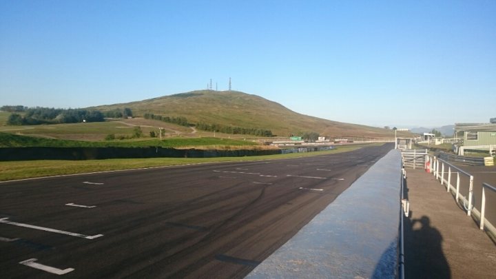 the bb trackday thread.   - Page 172 - Biker Banter - PistonHeads - The image depicts a large motorway adjacent to a grassy hill. The road is empty with no visible traffic or vehicles. The sky is clear and blue, indicating good weather conditions. In the distance, silhouettes of buildings can be seen against the skyline, suggesting a nearby town or city. The surrounding landscape appears serene, with a sense of openness that extends beyond the immediate motorway scene.