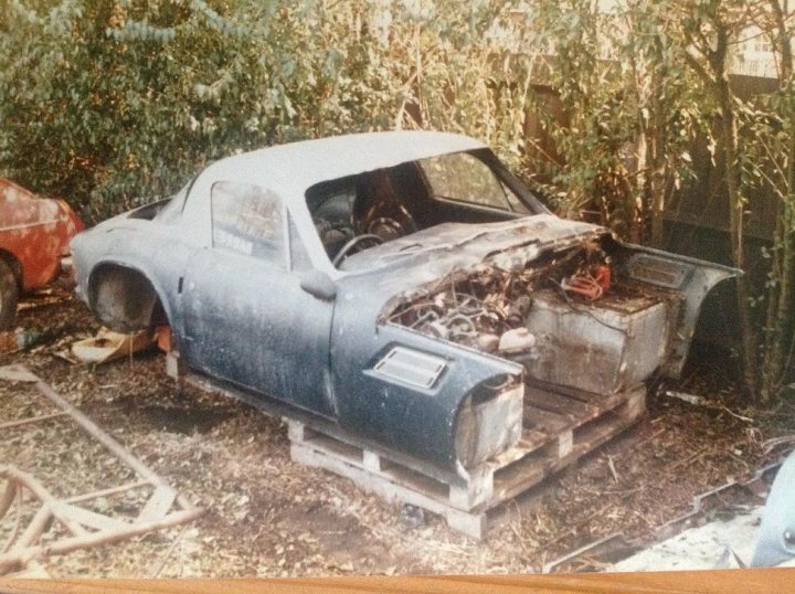 HOY 11K 4wd TVR se restoration project - Page 1 - General TVR Stuff & Gossip - PistonHeads - In the heart of a lush wooded area, under the cover of a serene sky, an old car is abandoned on a dilapidated pile of wood. The vehicle, once white, now bears the marks of time. Its trunk is open, revealing a trove of jumble and debris. The car sits next to a pile of spare parts, scattered with rust and piled high against its front. The scene is one of abandonment, a snapshot of a moment frozen in time.