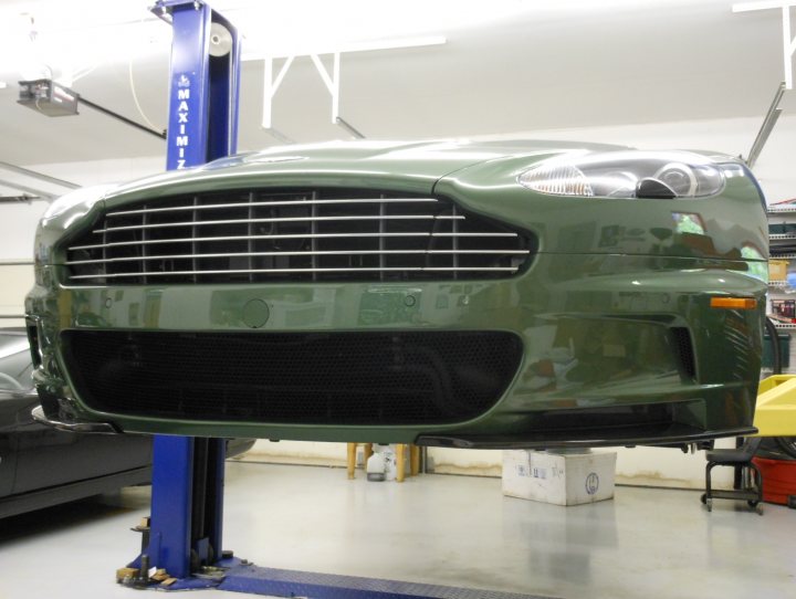 An airplane is parked in a parking lot - Pistonheads - This is an image of a car inside a garage or workshop. The car appears to be a shade of green or possibly a dark metallic color, and it is elevated on a lifting platform, suggesting that it might be undergoing maintenance or service. The platform on which the car is resting has blue and red safety markings. In the background, there are other vehicles, tools, and some boxes, indicating a commercial or professional setting typically used for vehicle repairs or maintenance. On the car's front grille, there is a prominent badge that resembles the Ford Mustang emblem.