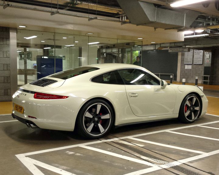 Supercars spotted, some rarities (vol 6) - Page 292 - General Gassing - PistonHeads - The image showcases a tilted view of a white Porsche Cayman parked in a parking garage. The car is positioned perpendicular to an empty parking spot with clear markings on the ground. The interior of the garage is visible, featuring ample natural light and well-suited architecture. The car's exterior appears to be a Cayman model, characterized by a sleek design and tasteful detailing. The overall scene suggests a quiet moment captured at the beginning of the day or during a less busy period.