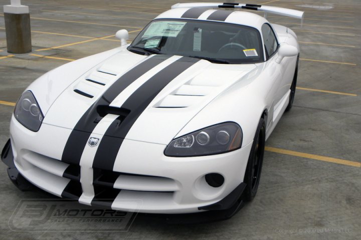 A car is parked on the side of the road - Pistonheads - The image shows a white convertible sports car parked in what appears to be a parking lot. The car is primarily white with black and white stripes running across its hood. It has a sleek, low-profile design typical of sports cars, and the top is lowered. A license plate or sticker is visible on the top-right side of the car's windshield. The car is the main subject of the photo.