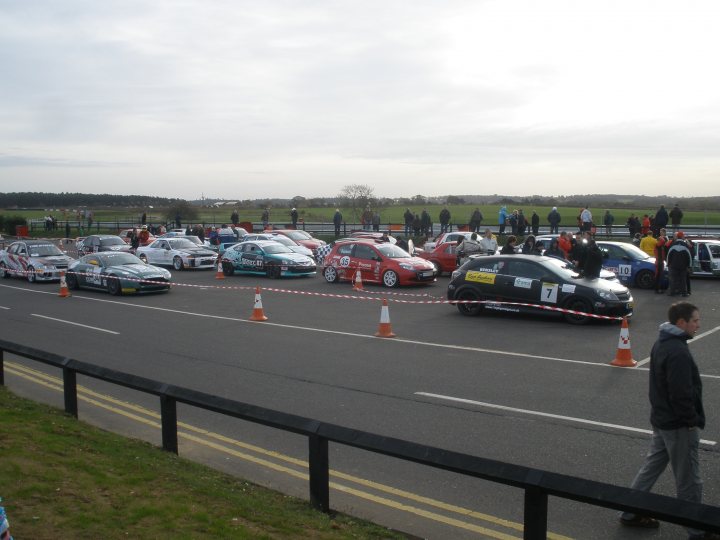 Thank you. - Page 1 - East Anglia - PistonHeads - The image shows an open roadway that is wide and provides plenty of space for vehicles to operate. Along this roadway, there is a stretch of paraded cars parked on their sides, creating a wide, inverted-V formation. These cars are various models and colors, suggesting a diverse gathering. Cones have been placed to section off the vehicles, indicating a planned event or display. At one end of the line, a large number of people have gathered, indicating their interest in the cars. The bright lighting and construction-like boundary suggest it could be a special event celebrating the cars or related to automotive testing or a race event.