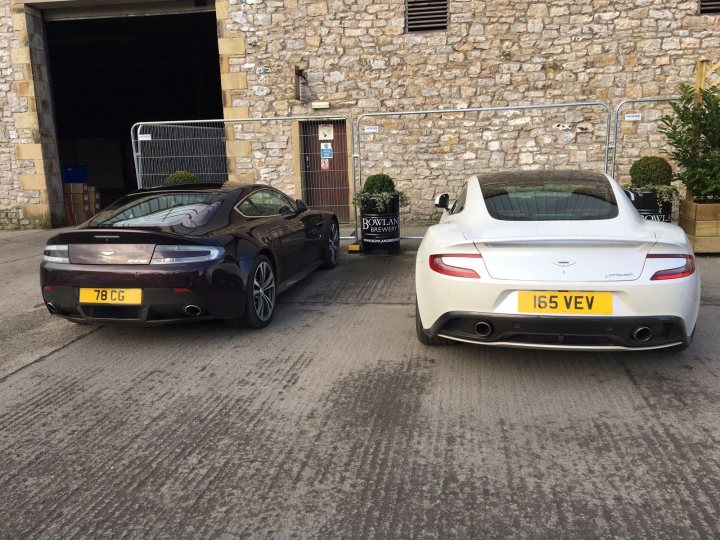 How about an Aston photo thread! - Page 1 - Aston Martin - PistonHeads - In the image, there are two convertible sports cars parked in front of a stone building, likely a house. The cars are positioned side by side, facing the same direction with their front ends visible. The left car is dark in color, possibly black or dark blue, while the right car is white. The license plates are visible and read "78 CG" and "165 VEV". The building adds a quaint backdrop to the automotive scene, and a small, green plant is situated in front of the building, adding a touch of nature to the otherwise urban setting.