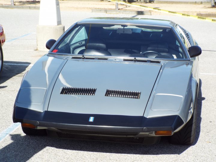 My 1972 De Tomaso Pantera - Page 3 - Readers' Cars - PistonHeads - The image shows a vintage sports car parked in a lot. It is a convertible with its top down, revealing the interior. The car's bodywork is in pristine condition, and it has a distinctive black-out grille and large air intakes on either side of the hood. A spoiler is mounted on the rear deck. The vehicle appears to be well-maintained and possibly customized or restored. It is parked next to another car, but only the sports car is in focus. The setting seems to be an outdoor parking area during daylight.