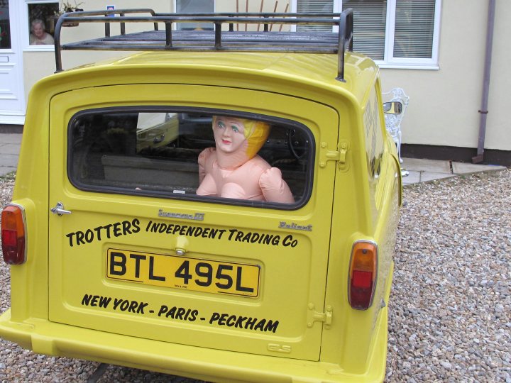 Landed Wij Towers Supercar Pistonheads - The image presents an eye-catching scene with a vibrant yellow trailer. The trailer is being used to advertise a business named 'Trotters Independent Trading Co.'. It is parked outside a house, and the tag reads 'BTL 495L'. Inside the trailer, there's an unusual sight - a doll,izarrely dressed in a pink helmet and butterfly wings. The license plate on the trailer reads "New York - Paris - Peckham", indicating a possible theme or affinity for these locations.