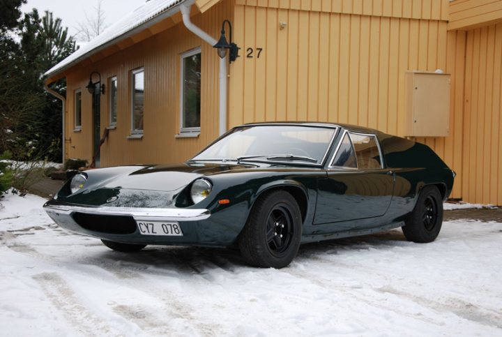 RE: Lotus Europa: Spotted - Page 5 - General Gassing - PistonHeads - The image showcases a teal or green vintage sports car parked in front of a yellow house. The car features a cleaningxy symbol indicating it is well-maintained. It has a black convertible top, matching wheels, and a notable track on the left side, suggesting it could be used for racing or high-performance road use. The vehicle is low to the ground, which is typical for sports cars, and it is parked on what looks to be a snowy driveway.