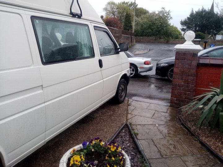 2004 Discovery TD5, a.k.a "The Bear Bus" - Page 2 - Readers' Cars - PistonHeads UK - The image shows a residential street scene. A white van is parked in front of the house, facing towards us. The van appears to be a commercial vehicle with visible branding and markings on its side. Next to the van, there is a small walkway leading up to the entrance of the house, which is not visible in the image.

The house itself is partially obscured by the parked van and other vehicles in front of it. The street is wet, indicating recent rainfall. There are multiple cars parked on both sides of the street, contributing to the crowdedness of the scene. The presence of a brick wall suggests that there might be some form of privacy barrier or fencing around the property.

The image seems to have been taken during the daytime, as indicated by the natural light and visibility of details. There are no visible people in the image, giving it a quiet and calm atmosphere. The overall impression is that of a typical suburban neighborhood.