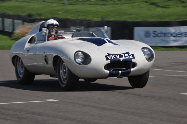 Goodwood yesterday...... - Page 1 - Classic Cars and Yesterday's Heroes - PistonHeads - The image depicts a vintage race car speeding down a track. The car is a silver sports car with a prominent VKV 752 registration plate. The head of a person can be seen through the steering wheel of the car, wearing a helmet and focused on the road ahead. In the background, a grassy area is visible with a partition bearing the Schroders logo. The setting suggests a professional racing event. The vehicle's sleek design is indicative of race cars from the era, with its streamlined body and minimalist decoration. The image captures the thrill and intensity of high-speed racing.