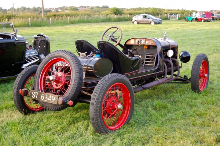 earls barton clasic car meet tomorrow april 24th  - Page 1 - Northamptonshire - PistonHeads - The image shows a field with vintage cars parked on the grass. One of these cars, which is the centerpiece of the image, is a shiny chrome and black Model T Ford. This vintage car is prominently displayed, occupying a large portion of the frame and essential to the composition. The rest of the field is adorned with other old cars, each with their own antique charm. The cars are parked in a line, their unique designs and vibrant colors suggesting a gathering or show of classic automobiles.