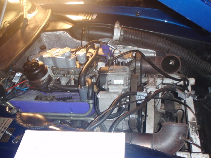 The image captures the intricate details of a car's engine, where various mechanical components are visible. The engine block, a solid piece of metal, is primarily blue and makes up the central part of the engine. It houses a throttle body and an air filter, essential components for regulating the airflow into the engine. Surrounding the engine block, you can see a collection of wires and hoses, intricately arranged to maintain the engine's performance. A fuel rail with multiple nozzles is also visible, ready to deliver fuel to the engine. The engine appears to be in good working condition, suggesting it may be a part of a well-maintained vehicle.