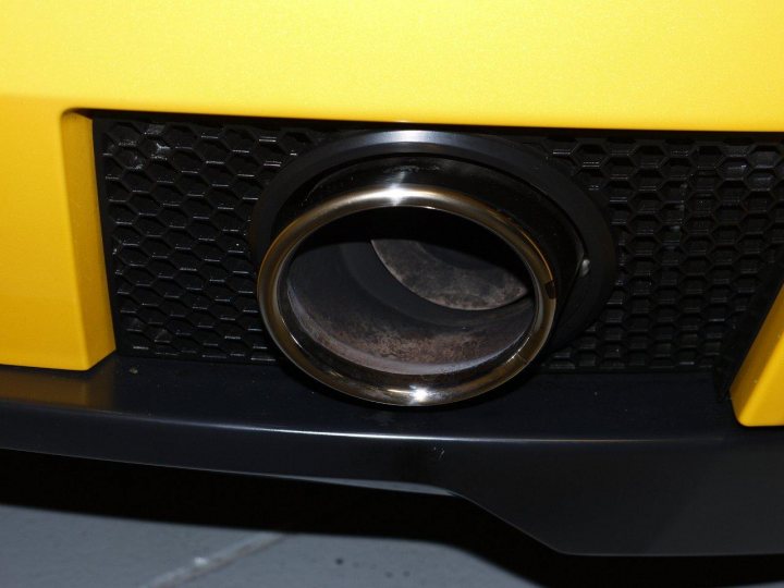 A close up of a computer mouse on a desk - Pistonheads - The image captures a close-up view of a yellow car's exhaust pipe. The exhaust pipe, painted black, showcases a silver oval-shaped component within it. This metallic component has become slightly scratched and tarnished, indicating exposure to elements and high temperatures. The precise location of the component is within the exhaust system, which is typically located under the vehicle to expel acquired pollutants. The expression of this component and its immediate surroundings exude a sense of griminess and robustness. The yellow color of the car contrasts sharply with the black and stainless components in the image, creating a visually striking difference in hues.