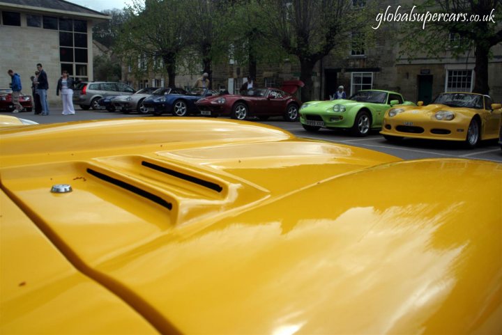 Sunday April 25th Bradford on Avon - Marocs - Page 1 - South West - PistonHeads - This image showcases an outdoor scene at a building, possibly a courthouse, where a row of brightly colored classic sports and marine sports cars are parked. The cars are parked close to each other and the variety of colors, such as yellow, red, and green, adds vibrancy to the scene. The setting is primarily made of concrete, and the building is partially visible in the background. There are a couple of people near the cars, which seem to be the main focus of this image. The branding "Global Supercars" is also visible in the top right corner, indicating that this could be a showcase or exhibition of luxury vehicles.