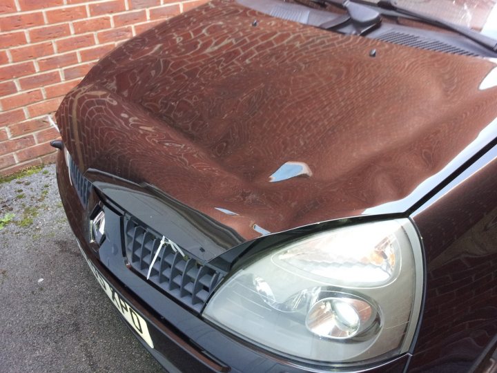 Pistonheads - The image showcases the front bumper of a black car that has seen better days. The bumper is damaged, with a large chip revealing the lighter underneath. Parts of the car's hood are also scratched and worn, indicating it has been exposed to rough conditions or a rough driver. The car is parked in front of a red brick wall, suggesting it's in an urban or industrial area. Despite the damage, the car's makeup focuses on functionality and utilitarian design.