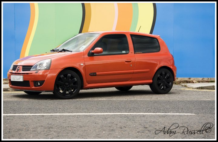 Thought Pistonheads Introduce - In the image, an orange car is parked on a street. The street seems to be relatively calm, with no other cars or pedestrians visible in the frame. Behind the car, there is a vibrant backdrop of a building with a striped wall and a blue wall. The car's color stands out against the background. The scene suggests a typical day in an urban area.