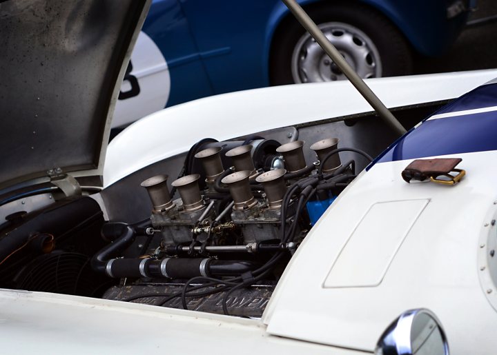 Robert Barrie Track Day 24th Feb Goodwood - photos - Page 1 - South Coast - PistonHeads - The image captures the profusion of mechanical parts that structure the interior of a vintage sports car. A distinctive blue and white GT model is identified, hinting at a specific make and model. The car's engine, housing various pipes and cables, reveals a complex web of machinery that underscores its historical appeal. The closed engine lid serves as a gateway, inviting the observer to step inside or gaze down upon this testament to automotive engineering. The surroundings hint at the presence of other vehicles, suggesting that the car is in a public setting or at a car show.