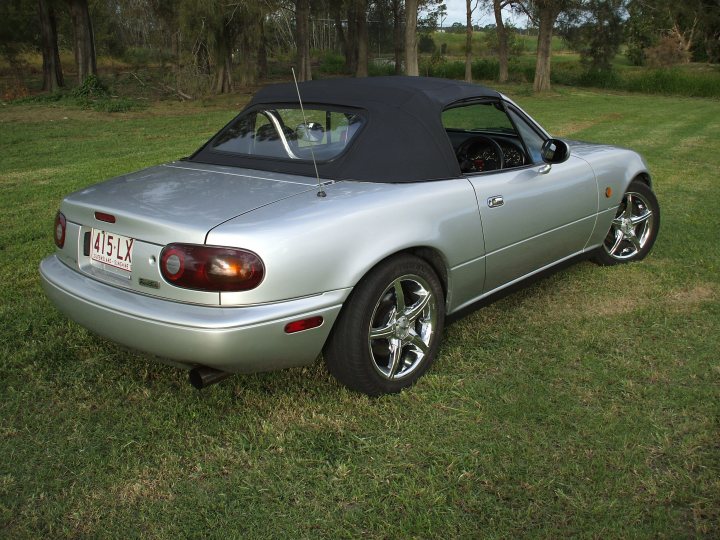 Spec Newbie Pistonheads Mazdaspeed Current - The image showcases a silver, two-door convertible parked on a grassy area. The car is facing the left side of the photo, and its top is up. The vehicle is equipped with alloy wheels and features a red taillight. In the background, there are trees and shrubs, adding a natural backdrop to the scene.