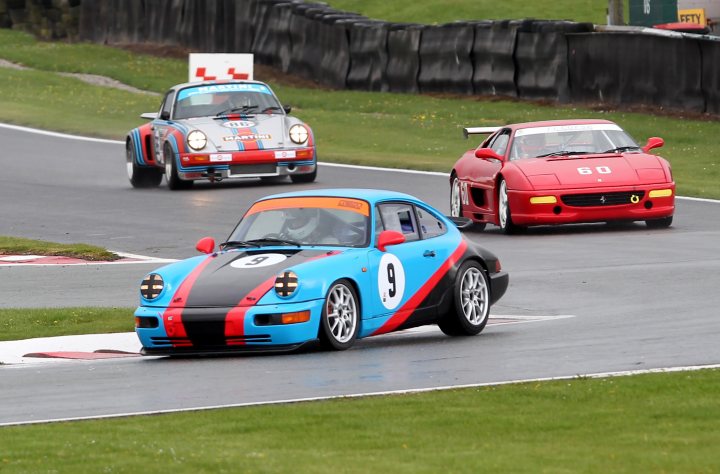 The annual what are you racing in 2014 thread.  - Page 1 - UK Club Motorsport - PistonHeads - The image captures an intense moment on a race track. Two cars are in motion, their speed evident by the blurred background. The first car, closer to the foreground, is a striking blue with red and white stripes on its hood and black and white stripes on its body. It bears the number 9 on its door. The second car, a bit further in the background, is red with a white rear wing and stripes on its hood as well, and it has the number 8 on its door. Both cars appear to be Porsche models, renowned for their racing heritage. The grassy area around the track can be seen in the corners of the image, providing a nice contrast to the grey tarmac of the track.