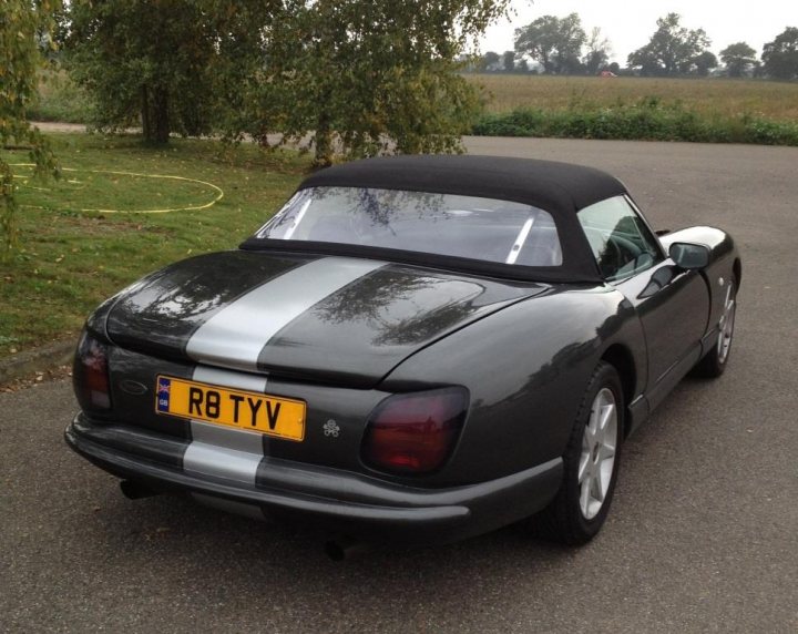 Vinyl Stripes - Norwich/Ipswich?? - Page 1 - East Anglia - PistonHeads - This image features a classic black and grey coupe parked on an asphalt surface. The car has a distinctive black roof and a white stripe running along the top. It features a license plate on the back that reads "R8 TYV". The setting appears to be an open field with a few trees and shrubs in the background. The sky is overcast, suggesting it might be a cloudy day.