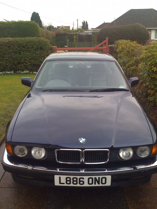 Shed Week Pistonheads - This image shows a dark-colored Bmw car parked in a driveway next to a grassy area with shrubs. The car features the BMW insignia on the grille and has tags indicating "L86 ONO." The vehicle is a two-door coupe with a sleek design and glass roof panels. The backdrop of the image includes a residential setting with other vehicles and houses, suggesting a quiet neighborhood during the day.