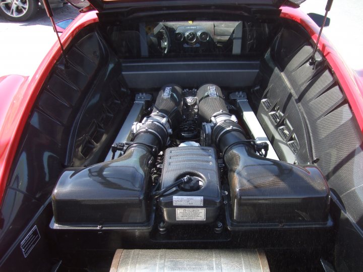 My First Ferrari...and its a Scud! - Page 1 - Ferrari V8 - PistonHeads - The image showcases the undercarriage of a convertible sports car. A prominent feature is the engine, which appears to be a turbocharged 2.3-liter four-cylinder unit. This engine setup is partially obscured by modern styling elements and a ground-hugging black underbody. The engine, car, and the bright reflection on the surface beneath it convey a scene of luxury and power. The car feature, tow hitch, is located towards the front right side of the image, providing a contrast to the complex mechanics of the engine.