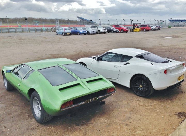 Some nice snaps - Page 1 - Evora - PistonHeads - The image showcases a parking lot scene with two cars parked adjacent to each other. The left side of the image is dominated by a lime green vintage car that appears to be a Mazda RX-7, known for its rotary engine. The right side features a white convertible, the make and model of which appear to be hidden in the vehicle's blind spots. Behind these cars, more vehicles are visible, indicating a public or semi-public parking area. The lot is devoid of any foliage, suggesting a setting with little vegetation. The overcast sky and the open setting give the scene a moody and somewhat nostalgic feel, characteristic of many automotive photography settings.