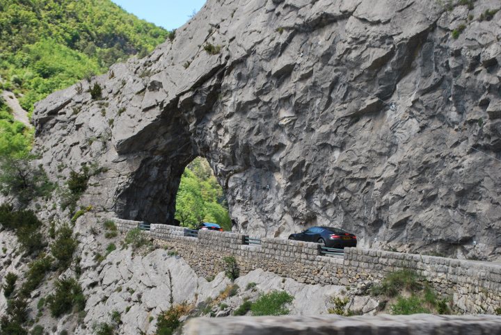 Pistonheads trip to Monaco Historique - Page 2 - Aston Martin - PistonHeads - The image captures a scenic highway carved into a massive, natural rock formation. Cars are traversing the winding, two-lane road, which is situated deep within a sizable mountain. The road seems to be a popular route among tourists, with multiple vehicles adding life and motion to the otherwise tranquil scene. The perspective of the photo suggests it was taken from the viewpoint of a visitor observing the rocky landscape and the cars on the road. This scene conveys a sense of adventure and respect for nature as man-made infrastructure is safely integrated into the rugged terrain.