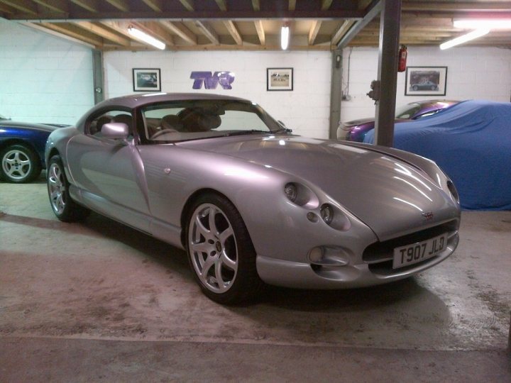 Cerbera Best Pic - Page 56 - Cerbera - PistonHeads - This image captures a garage scene with a silver sports car parked prominently. The car is sleek and modern, boasting a gleaming pearl white finish. Its flat gray roof contrasts with the car's silver body. The license plate sports the text "TVO LJL", indicating the car's registration. The garage setting is further decorated by the presence of other cars and various decorative elements on the walls.