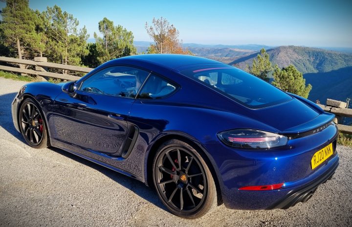 Pistonheads - The image is a split-screen photograph showing the front and side of a blue sports car. The vehicle is a modern model, possibly a Porsche or Audi, given its sleek design and badging. The car's bodywork appears to be in excellent condition, with no visible damage or scratches. It has large, alloy wheels and a prominent rear spoiler.

The top half of the image is slightly blurred, while the bottom half provides a clearer view of the vehicle's side profile. The car is parked on a paved surface, suggesting that this might be taken during a road trip or a casual photo session. There are no people visible in the image. The background consists of a natural landscape with trees and hills, indicating that the location may be rural or near a mountainous area. There's also a clear sky above, which suggests it could be a pleasant day for outdoor activities.