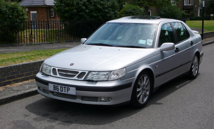 A white car parked in a parking lot - Pistonheads - The image showcases a silver sedan parked on the side of a road. The car has a European-style license plate featuring the letters "B6 DTP". The vehicle is parked next to a sidewalk, and it appears to be well-maintained. In the background, there are houses and trees, providing a suburban setting. Additionally, there is a person visible in the image, although they do not seem to be interacting with the car.