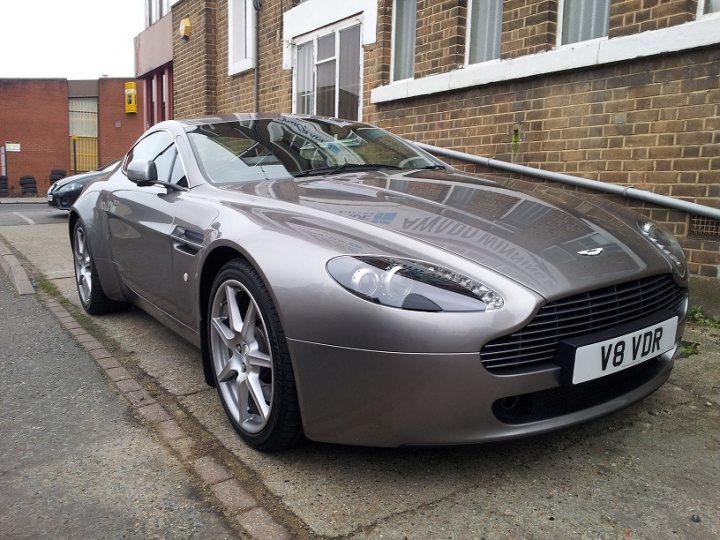 Another fully fledged member - Page 1 - Aston Martin - PistonHeads - The image captures a sleek silver sports car parked on a brick sidewalk in front of a brick building. The car's long hood and short rear tail give it an aggressive and aerodynamic stance. A notable feature is the state license plate that reads "V6 VDR". The car is parked parallel to the curb, with some space between it and the building.

The brick building in the background adds an urban feel to the scene, while the cars parked behind the sleek sports car ground the image in a real-world setting. The image exudes an urban, sophisticated air, highlighted by the architecture of the building and the imposing presence of the luxury car.