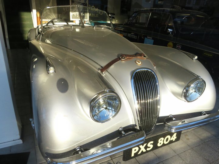 Pistonheads - The image showcases a classic, silver Jaguar car displayed in a shop. The car is parked near the front of the store, with its hood open, allowing one to admire its engine. A display case with a glass top is situated behind the vehicle, adding an air of sophistication to the scene. There are other cars visible in the background, suggesting that this establishment specializes in vintage or classic vehicles. The overall atmosphere suggests a place where enthusiasts can appreciate and learn about these automotive marvels.