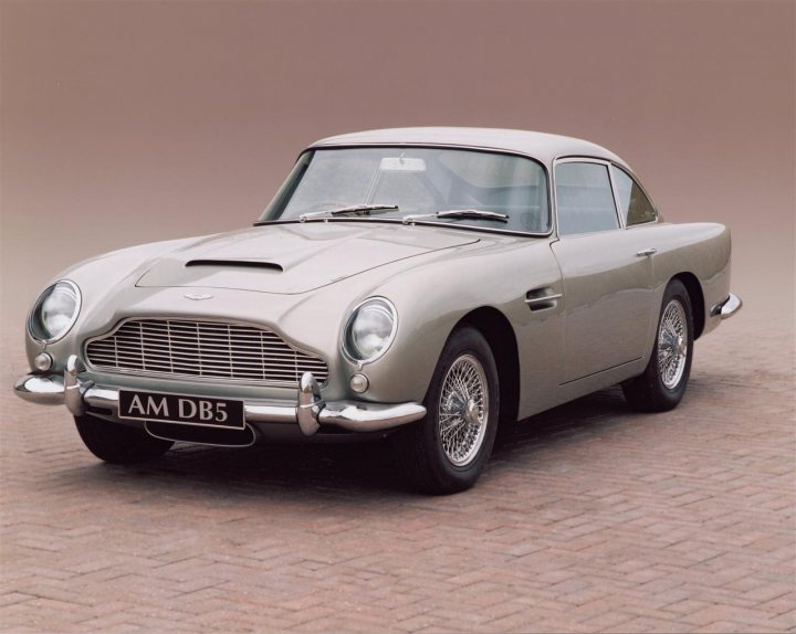 Your favourite car from the year you were born in... - Page 12 - General Gassing - PistonHeads - The image depicts an Aston Martin DB5, a classic and iconic grand tourer car produced between 1963 and 1967. The car is shown in profile, with its distinctive streamlined design, long hood, and short rear deck. It has a prominent front grille and side vents, which are characteristic features of the DB5. The wheels have silver hubcaps and wire wheels, which adds to the car's vintage aesthetic. The car's color scheme consists of a silver body with a gray interior, and the license plate reads "AM DB5".