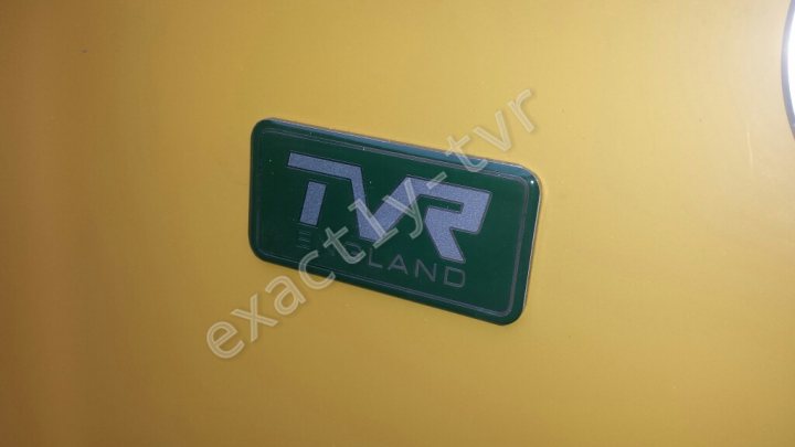 A close up of a street sign with a sky background - Pistonheads - The image captures a close-up view of a green sticker affixed to a wall, which is a bright yellow, indicating an area of interest or activity like a station, store, or facility. The sticker features white lettering, likely the name or logo associated with a travel route. The reflection of another area or space can be seen in the bottom right of the image.