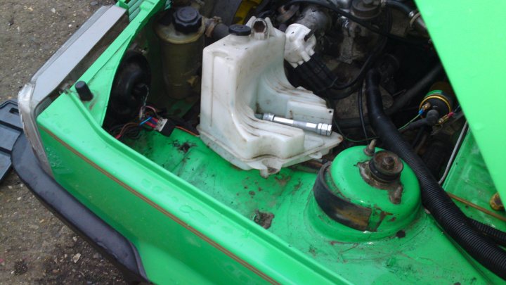 Sublime Pandamonium II - Page 32 - Alfa Romeo, Fiat & Lancia - PistonHeads - The image shows the engine bay of a vehicle that is predominantly green. A white plastic container is visible on the right side of the vehicle's engine compartment. There appears to be wiring near the container and the engine. The environment suggests the engine is under the hood of the vehicle, and the setting seems to be an outdoor, rough ground area. There is also a battery in the frame.