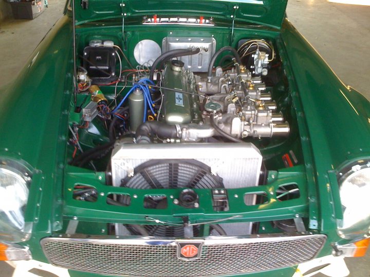 Pistonheads - The image shows a vintage-style car with a dark green paint job. The vehicle is lifted, predominantly displaying the engine compartment. The engine is highly visible, with numerous cylinders, belts, and metal components visible. The engine is paired with a cooling fan in front. A Mercedes emblem is prominently displayed, suggesting the make or model of the car.