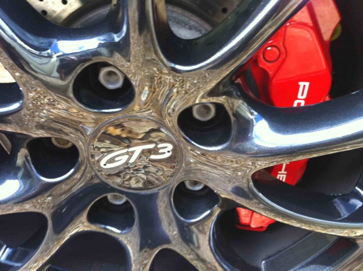 Pics you just love - Page 24 - Porsche General - PistonHeads - The image captures a close-up view of the rear wheel of a car. The center hub cap is prominently visible, displaying a white car company logo. Inside the hub cap, you can see its silver metal structure. The tire is casting a slight shadow, providing depth to the image. The car is parked, and the environment suggests it's an outdoor setting.