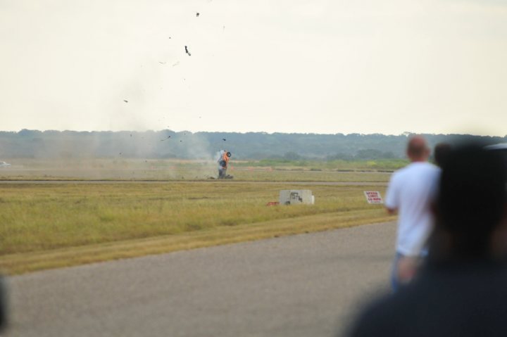 Gallardo Pistonheads Mph Crash - This image captures a dynamic scene at an airport taxiway. A person is jogging along the runway, with a noticeable plume of dirt or debris visible behind them. An airplane is in the background, suggesting the taxiway's active use. A sign with red text is partially visible, but the text is not legible. Other people are walking near the foreground, contributing to the bustling atmosphere of the scene.