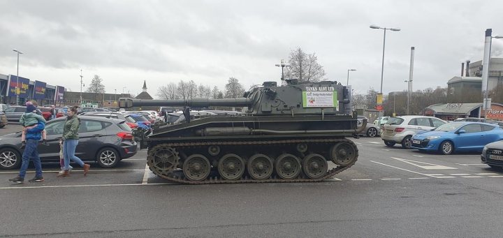 Local Facebook groups - Page 507 - The Lounge - PistonHeads UK - The image shows a military-style tank parked in what appears to be a parking lot. The tank is large and imposing, with the words "KRUGGERAND" visible on its side, suggesting it may belong to the Swedish army or have been used in Swedish military operations. The background reveals a typical urban setting with cars, buildings, and people present, indicating that this scene might be from a public event where the tank is being displayed for public viewing.