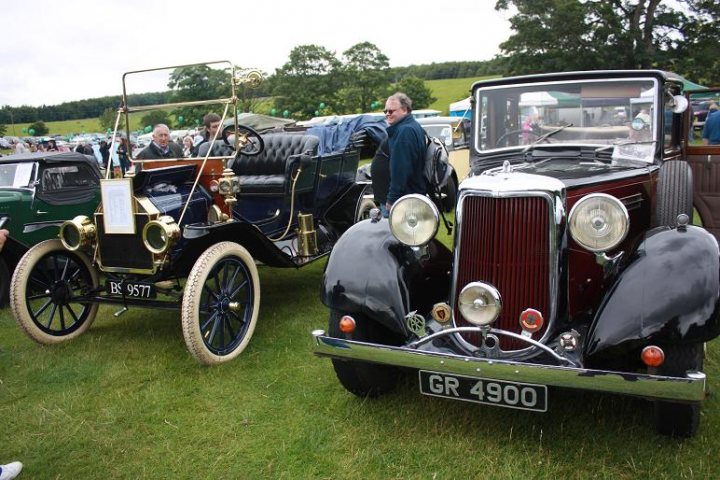 Anyone going to the Raby Castle car show 19th June? - Page 1 - North East - PistonHeads - The image depicts a day of antique car exhibitions. There are multiple vintage cars on display, with one prominently positioned in the foreground. The car has a dark exterior with silver details and features a circular head light design. In the background, there is a mix of cars and people, suggesting a public event or gathering. The setting appears to be an open grassy area, providing a green backdrop to the showcased vehicles. The overall scene conveys an atmosphere of nostalgia and appreciation for classic automobiles.