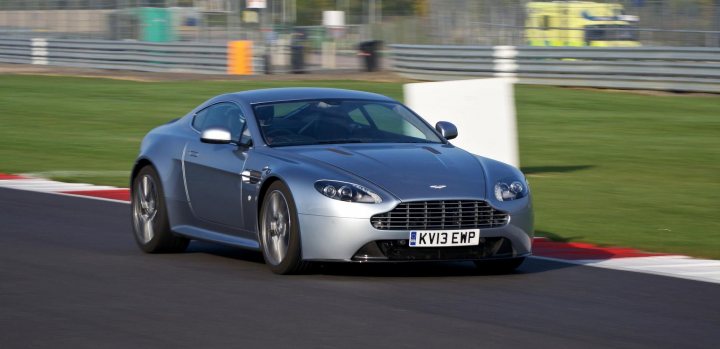 So what have you done with your Aston today? - Page 226 - Aston Martin - PistonHeads - The image captures a dynamic scene on a race track. A sleek gray sports car, adorned with a license plate that reads "KV13 EMP," is seen maneuvering around a corner. The car's speed is palpable, as evident from the blur that accompanies it. The race track itself, marked in black and white, provides a stark contrast to the car. The backdrop consists of a grassy field, a guardrail, and a building, adding depth and context to the scene. The image is a blend of motion and stillness, with the stationary elements positioned symmetrically on the sides, providing bookends to the fast-paced action at the center.