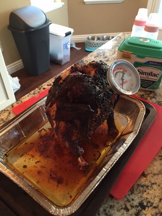 The bbq photo & recipe thread - Page 111 - Food, Drink & Restaurants - PistonHeads - The image features a clear aluminum tray with a bird sitting in it. The bird appears to be seasoned with a black rub, and it's placed on a red placemat. The tray is resting on a kitchen countertop with a wooden base. The countertop is well-lit, showing the bird, tray, and placemat in detail. In the background, a part of a trash can can be seen, indicating a domestic setting.