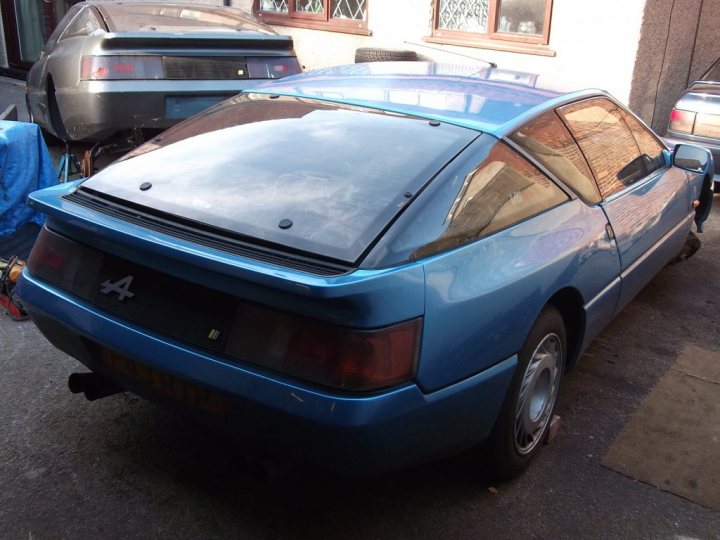 A blue car parked next to a parking meter - Pistonheads - The image features a pristine blue sports car parked in a driveway next to a silver coupe. The car showcases a sleek and polished design with a spoiler and exhaust pipe visible. The driveway setting, with the vehicles positioned in front of a house, suggests a residential area. Despite the presence of a red reflector on the back of the blue car, the car itself is without license plates.