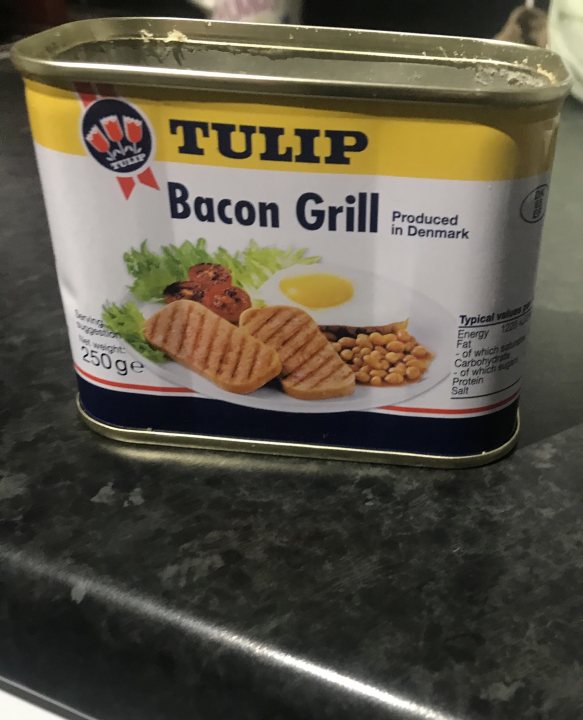 The Great Breakfast photo thread - Page 352 - Food, Drink & Restaurants - PistonHeads - The image shows a can of "Tulp Bacon Grill" prominently displayed, with an image of food items that resemble chicken pieces and possibly vegetables or salad. The can is placed on a kitchen countertop, which has a dark surface and appears to be made of wood. There are no people visible in the photo, focusing attention solely on the product. The background is simple and does not distract from the main subject, which is the canned food item.