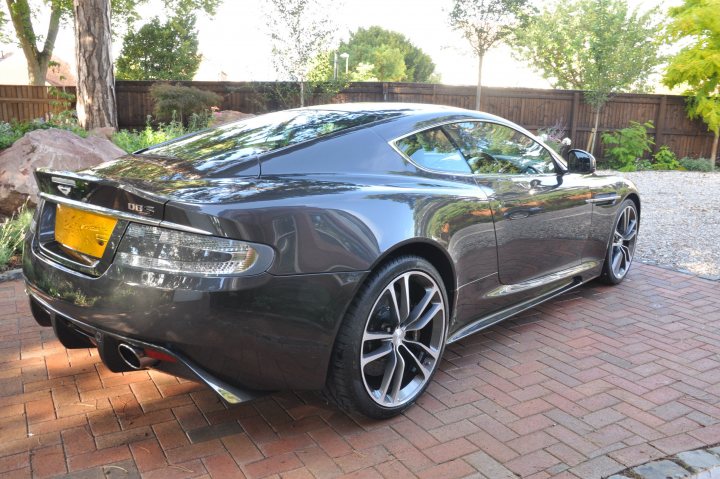 Dbs Pistonheads Finally Vantage - The image shows a sleek and modern sports car parked outdoors. The car, with its metallic silver body and glossy black wheels, exudes an air of elegance and power. A black license plate is mounted on the rear, providing a contrast to the car's shiny exterior. The background features a brick driveway, a wooden fence, and sparse greenery, indicating a private or residential setting. The weather appears to be clear and sunny, casting soft shadows on the car and the ground. The overall composition of the image suggests a calm and tranquil atmosphere.