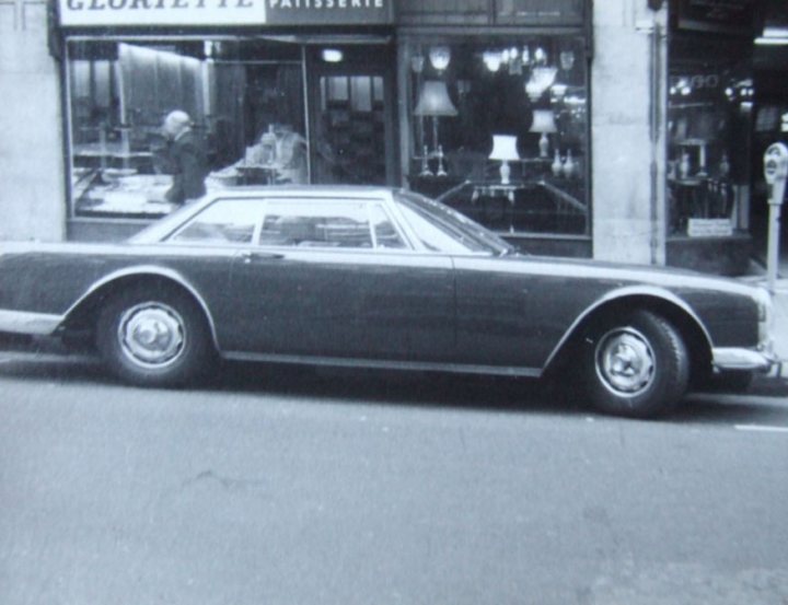 Help Facel Vega, Facel 2 - Page 37 - Classic Cars and Yesterday's Heroes - PistonHeads - The image showcases a classic car positioned on a city street in front of a patisserie. The car, sleek with a long bonnet and low rear wheel, appears to be from the 1960s, featuring the friendly round headlights that were characteristic of that era. The patisserie itself has a welcoming ambiance, with a large window on the ground floor and lighted lamps providing a cozy atmosphere. A parking meter is visible on the sidewalk next to the car, suggesting a well-regulated parking system in the city. The photograph itself has a vintage quality, with a faded effect that contributes to the timeless feel of the scene.