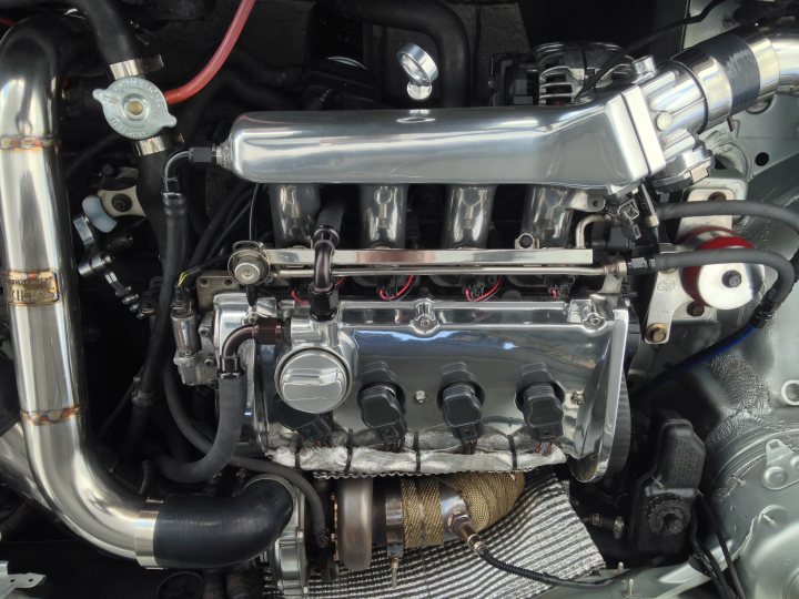 Daily driven 500bhp Golf - This image provides a comprehensive view of the mechanical workings underneath the hood of a car. The engine, the heart of the vehicle, is on display, revealing an intricate network of pipes and wires that are the essence of internal combustion. There's an abundance of tubing, some of which are black and others stainless steel, running throughout the engine bay. The engine itself features a five-port manifold, with four distinct vents and a single large chamber emitting a soft glow. The entire structure is organized in such a way that everything seems in place, reflecting the precision and complexity inherent in automotive engineering.