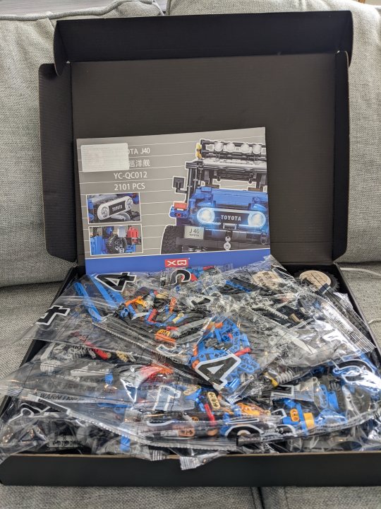 The LEPIN "LEGO" for non sensitive types - Page 122 - Scale Models - PistonHeads UK - The image presents a neatly organized box filled with an assortment of toy cars. Each car, varying in colors and designs, is carefully placed within the confines of the box. On top of the box, there's a manual that presumably provides guidance or information about the toy cars inside. The box appears to be newly unboxed, as suggested by the opened state and the array of toys visible through the packaging material.